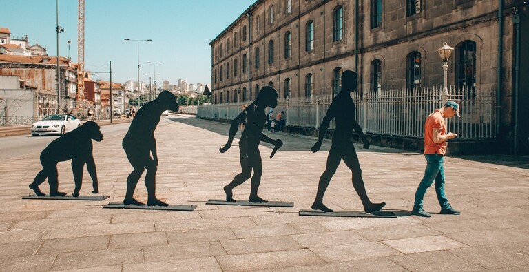 A man standing next to four figures showing the evolution of humans from apes