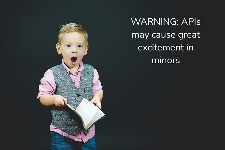 Child in a pink shirt and gray vest holding a book with a look of surprise on his face, with overlayed text that says "Warning: APIs may cause great excitement in minors"